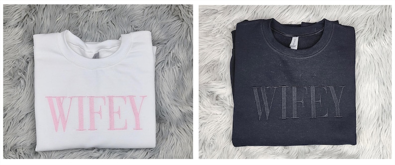 May include: Two sweatshirts with the word "WIFEY" printed on them. One sweatshirt is white with pink lettering and the other is dark gray with black lettering.