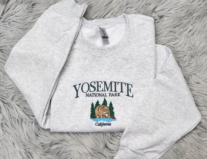 May include: A gray sweatshirt with the text "Yosemite National Park" and an embroidered image of a bear in a forest setting. The text "California" is below the image.
