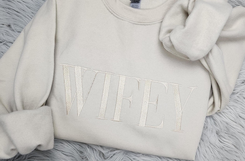 May include: A cream-colored sweatshirt with the word "WIFEY" embroidered in white thread.
