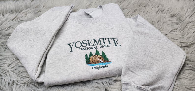 May include: Gray sweatshirt with a green embroidered design that says "Yosemite National Park" with a bear and trees. The text "California" is below the design.