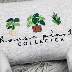 Puede incluir: Sudadera gris con plantas de interior bordadas y el texto "house plant collector".