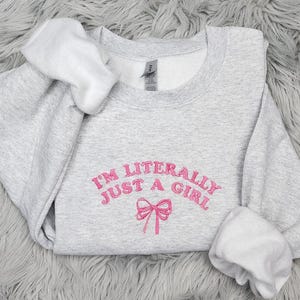 May include: Gray sweatshirt with the text "I'm literally just a girl" in pink lettering and a pink bow.