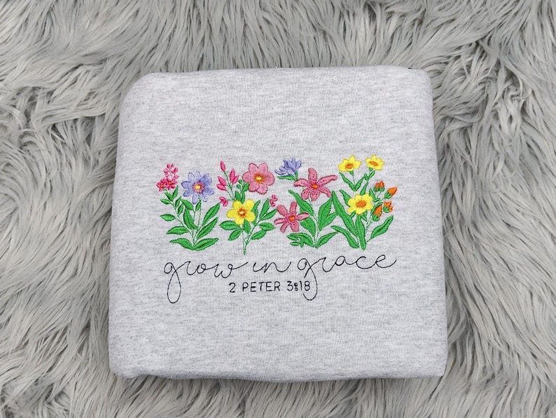 以下が含まれることがあります： グレーのトレーナーに刺繍された花と「grow in grace 2 Peter 3:18」の文字。
