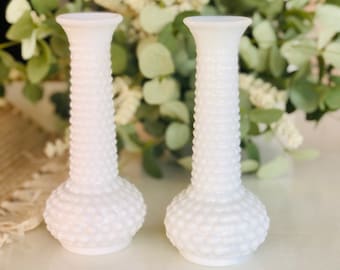 Può includere: Due vasi per boccioli in vetro di latte bianco con un design testurizzato e a bolle. I vasi sono alti e sottili con una base arrotondata.