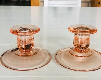 May include: Two pink glass candle holders with a simple design. The holders have a round base and a cylindrical center.