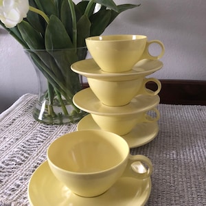 May include: A set of four yellow ceramic teacups and saucers. The cups and saucers are stacked on top of each other.