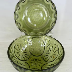 May include: Two green glass bowls with a decorative pattern. The bowl on top has a scalloped edge and the bowl on the bottom has a starburst pattern.