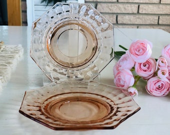 May include: Two pink glass octagonal saucer plates with a raised rim and a scalloped edge. The plates are stacked on top of each other.