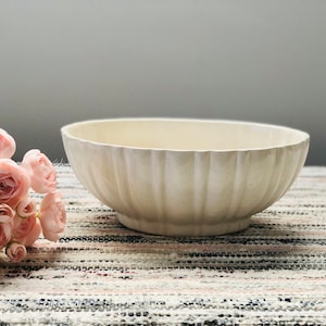 May include: A white ceramic bowl with a fluted design. The bowl is sitting on a striped rug.