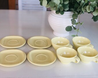 May include: A set of six pale yellow teacups and saucers. The cups and saucers are all the same size and shape. The cups have a rounded shape and the saucers have a slightly flared edge. The cups and saucers are all made of a smooth, glossy material.