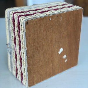 May include: A woven storage box with a wooden base. The box is made of natural straw with burgundy stripes.