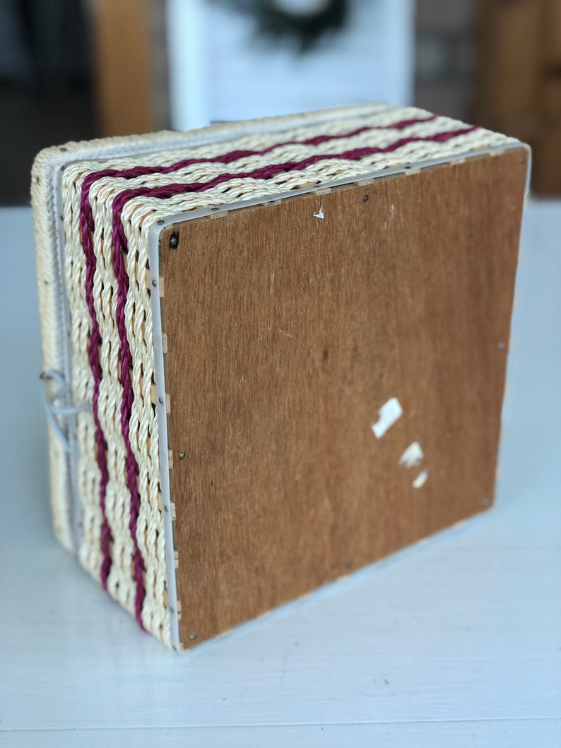 May include: A woven storage box with a wooden base. The box is made of natural straw with burgundy stripes.