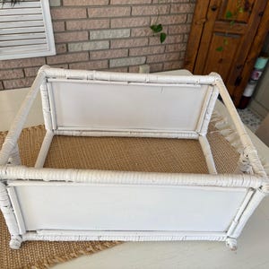May include: A white wicker serving tray with a rectangular shape. The tray has a woven base and a handle. The tray is on a white table with a woven runner.