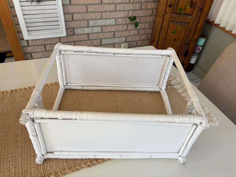 May include: A white wicker serving tray with a rectangular shape. The tray has a woven base and a handle. The tray is on a white table with a woven runner.