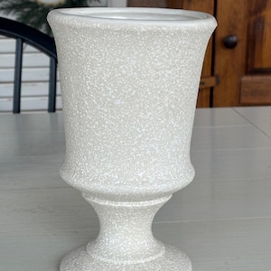 May include: A white ceramic vase with a speckled finish. The vase has a wide base and a narrow neck.