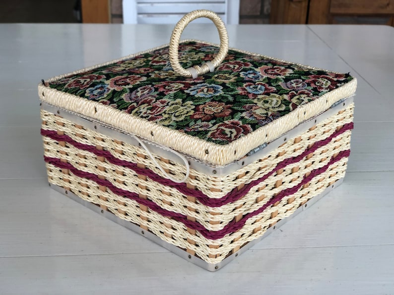 May include: A woven wicker storage box with a floral fabric lid and a metal ring handle. The box has a cream and burgundy color scheme.