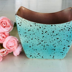 May include: A turquoise ceramic planter with black speckles. The planter has a curved, rectangular shape.