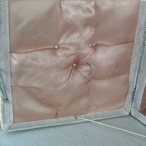 May include: A white fabric box with a white lace trim and a pink satin lining. The box has four buttons on the inside of the lid.