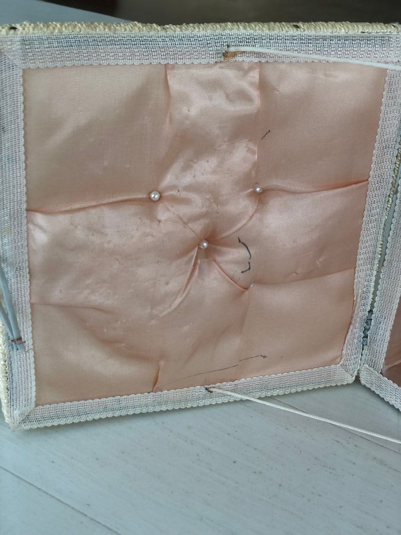May include: A white fabric box with a white lace trim and a pink satin lining. The box has four buttons on the inside of the lid.