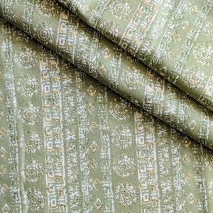 Op de afbeelding: Groene stof met een wit en gouden geometrisch patroon. De stof is dubbelgevouwen, waardoor het patroon aan beide kanten zichtbaar is.