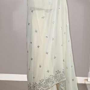 May include: A white chiffon saree with silver embroidery and sequins. The saree has a floral design and is perfect for special occasions.