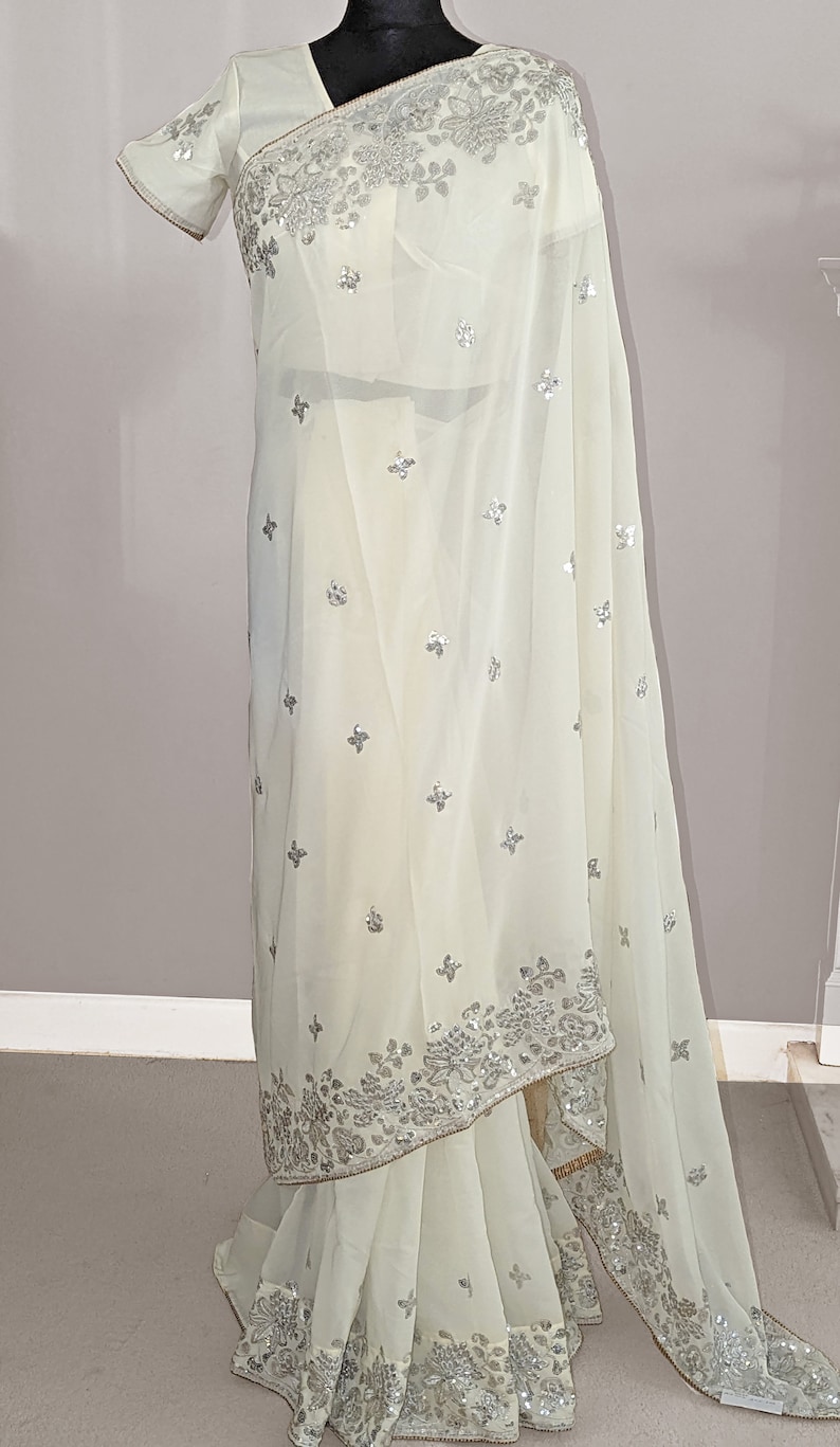 May include: A white chiffon saree with silver embroidery and sequins. The saree has a floral design and is perfect for special occasions.