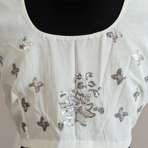 May include: A white blouse with a scoop neck and short sleeves. The blouse is decorated with silver sequins in a floral pattern and butterfly shapes.