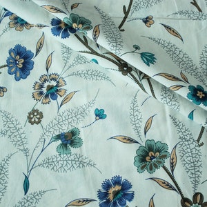 Peut inclure: Tissu blanc avec un motif floral bleu et vert répété. Le tissu a un léger brillant et une texture douce.