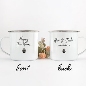 May include: Two white enamel mugs with black text and a pine cone design. The front mug says "Happy Tin Years" and the back mug says "Alan & Jackie 09-23-2013".