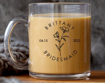 May include: A clear glass mug with a black design that says "Brittany Bridesmaid 04.15.2022" with a floral illustration.