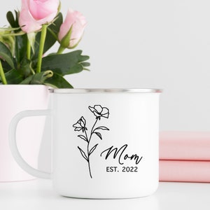 May include: White enamel camping mug with a black outline of a flower and the text "Mom Est. 2022".