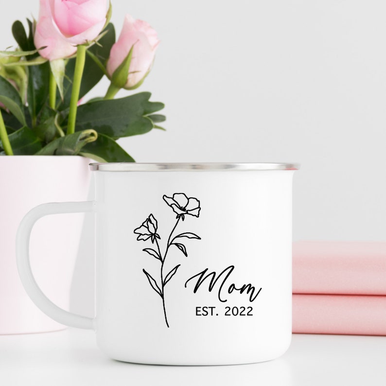 May include: White enamel camping mug with a black outline of a flower and the text "Mom Est. 2022".