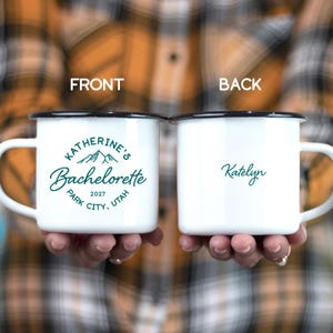 May include: Two white enamel mugs with black rims and handles. One mug has "Katherine's Bachelorette" with mountain graphic and "Park City, Utah 2027" in teal. The other mug has "Katelyn" in teal.