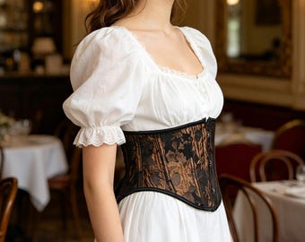 May include: A white dress with a square neckline and puff sleeves is paired with a black and bronze floral corset. The corset has a detailed pattern and is cinched at the waist. The outfit is reminiscent of historical fashion.
