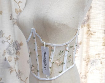 May include: White mesh corset with floral embroidery and a white satin ribbon. The corset has a label that reads "Dilkesshop on Etsy".