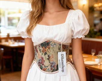 May include: A white dress with a square neckline and short, puffy sleeves. A floral tapestry corset with a light pink trim is worn over the dress. A tag that says "DikesShop on Etsy" is attached to the corset.