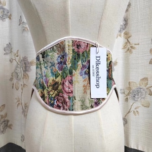 May include: A floral tapestry corset with a cream-colored trim and a tag that reads "Dikesshop on Etsy." The corset is displayed on a mannequin. The floral pattern includes pink, blue, and green hues.