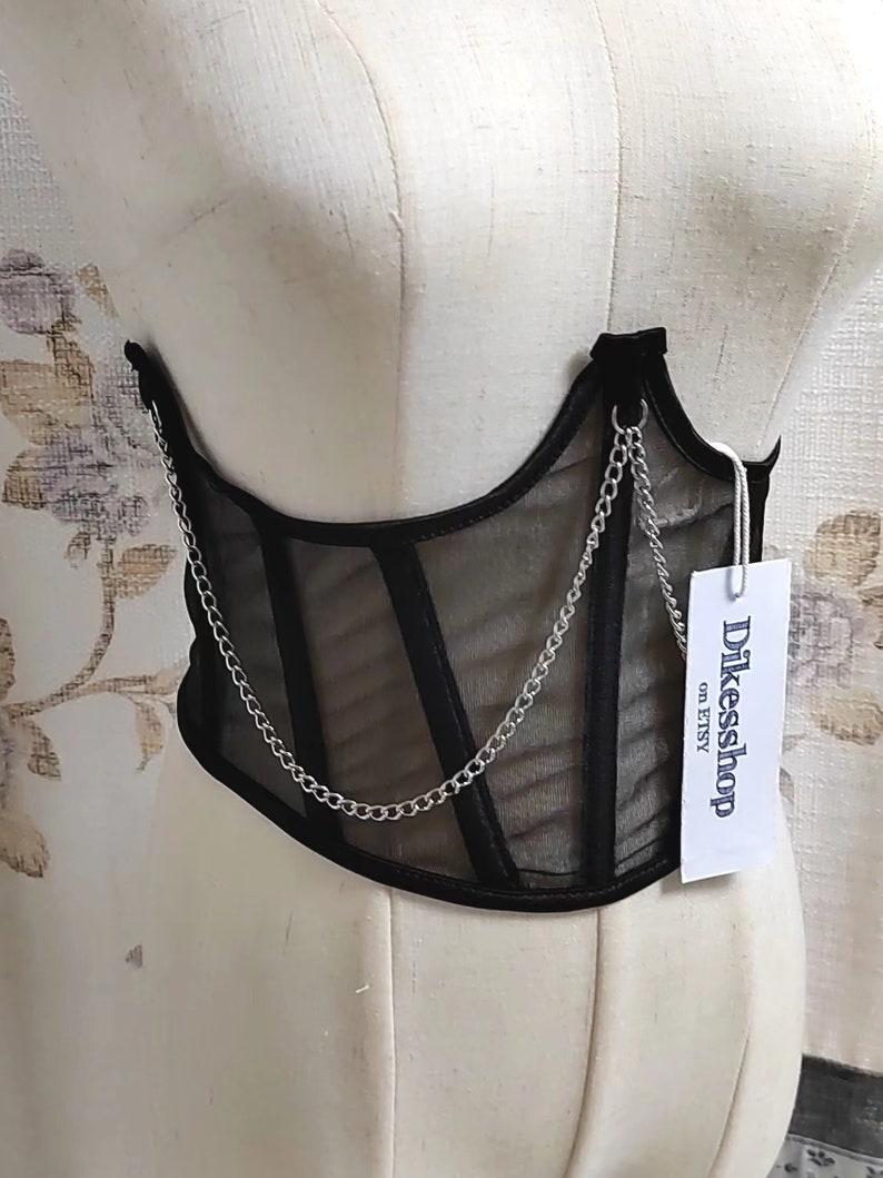 K&ouml;nnte beinhalten: Schwarzes Mesh-Korsett mit silbernem Kettendetail. Das Korsett hat ein Etikett mit der Aufschrift "Dikessshop on Etsy".