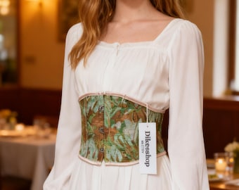 May include: A white long-sleeved dress featuring a square neckline and a structured corset-style waist belt. The belt has a green and brown floral tapestry pattern with three front buttons and a white tag labeled Dikesshop.