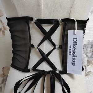 K&ouml;nnte beinhalten: Schwarzes Mesh-Korsett mit Satinband-Schn&uuml;rung und silbernen Metallringen. Das Korsett hat eine schwarze Satinband-Schleife auf der R&uuml;ckseite. Das Etikett lautet "Dikeshop on Etsy".