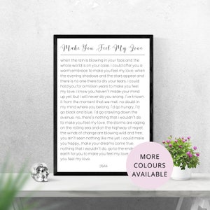 May include: A printable wall art print with a black frame and white text. The text reads "Make You Feel My Love" and includes a song lyric about love. The print has a pink and white "More Colours Available" label in the bottom right corner.
