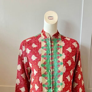 May include: A long, red quilted jacket with a green and white geometric pattern down the front. The jacket has a mandarin collar and a button closure.