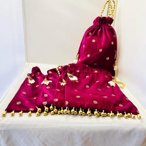 May include: A set of three magenta velvet pouches and a drawstring bag. The pouches have gold beaded trim and small gold floral embroidery. The drawstring bag has a gold beaded handle and matching embroidery.