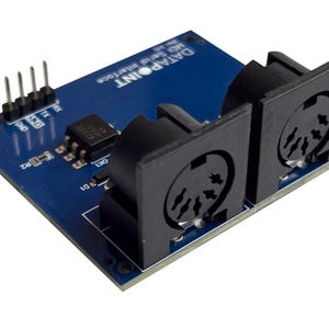 Könnte beinhalten: Eine blaue DATAPOINT MIDI Serial Interface-Leiterplatte mit schwarzen Anschlüssen und Stiften. Die Platine trägt den Text "DATAPOINT MIDI Serial Interface". Die Platine hat mehrere elektronische Komponenten.