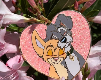 May include: A heart-shaped pin featuring the animated characters Tramp and Angel from Lady and the Tramp. The pin has a pink glitter background and a gold border. The characters are in a loving embrace.