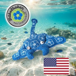 以下が含まれることがあります： 手作りの青いかぎ針編みのエイ。白いアクセントと詳細なパターンが特徴です。ぬいぐるみは白い丸い目と長い直立した尾を持っています。画像にはテキストとアメリカ国旗のロゴが含まれています。