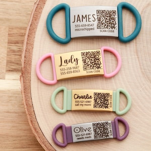 May include: Four pet ID tags in teal, pink, mint green, and purple. Each tag has a name, phone number, and a QR code. The teal tag says "JAMES", the pink tag says "Lady", the mint green tag says "Charlie", and the purple tag says "Olive".
