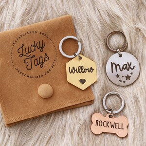 May include: Three personalized pet ID tags with a brown velvet pouch. The tags are engraved with the names "Willow", "Max", and "Rockwell". The pouch has the text "Lucky Tags" and "Personalized for Pets" printed on it.