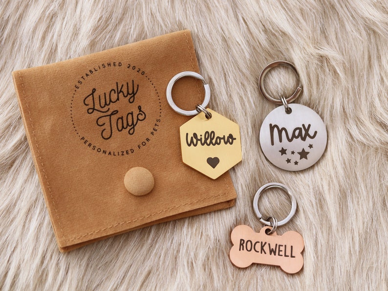 May include: Three personalized pet ID tags with a brown velvet pouch. The tags are engraved with the names "Willow", "Max", and "Rockwell". The pouch has the text "Lucky Tags" and "Personalized for Pets" printed on it.