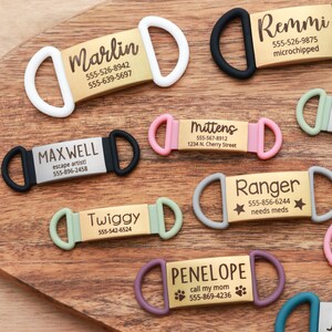 May include: A collection of personalized pet ID tags in various colors, including white, black, pink, green, and purple. Each tag features a name and contact information, with some including additional details like "microchipped" or "needs meds."